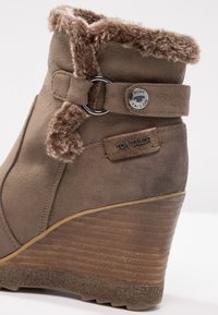 Botte compensée à cheville en suédé marron avec bordure en fausse fourrure, anneau en métal et bouton ainsi qu'étiquette de marque Tom Tailor sur le côté.