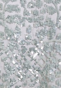 Tissu à sequins vert clair et argenté. Présente des sequins circulaires disposés en motif floral sur un fond en maille blanche.