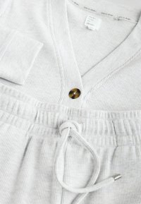 Light gray loungewear set with a textured ribbed fabric, featuring a buttoned top and drawstring waistband, accented by a contrasting button.