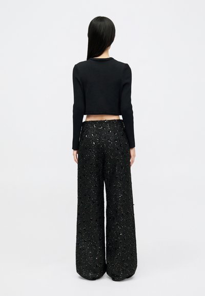 Un haut court à manches longues noir associé à un pantalon large noir en sequins avec des textures variées et des détails scintillants tout au long.