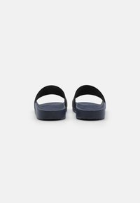Mørkeblå sandaler med en teksturert fotbed, glatte svarte stropper og et minimalistisk design. Sålen har riller for grep.