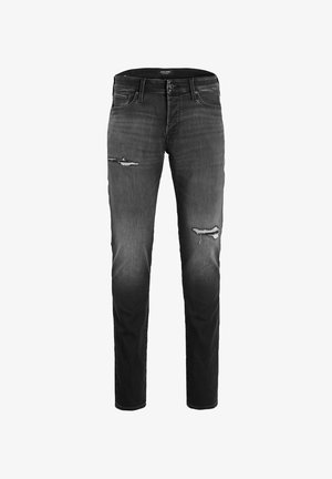 Młoda osoba ubrana w granatowo-czarną pikowaną kurtkę, czarne podarte dżinsy oraz czarne wysokie trampki ze sznurówkami i spodem w kolorze białym.