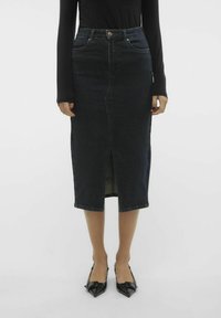 Mörk tvättrad midikjol med en slits framtill, utrustad med fem fickor och en figurnära silhuett. Kombineras med svarta pumps.