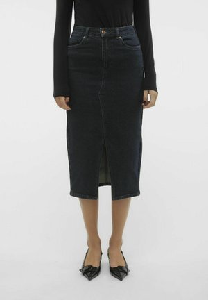 Jupe midi en denim foncé avec une fente à l'avant, comportant cinq poches et une silhouette ajustée. Associée à des chaussures noires à bout pointu.