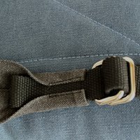 Gray fabric strap with metal buckle attached to a textured blue material, showcasing stitching details and an angled design.