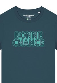 Dunkelblaues T-Shirt mit kurzen Ärmeln, das "BONNE CHANCE" in fetten, türkisfarbenen Buchstaben zeigt. Weiches, glattes Material; runder Ausschnitt.