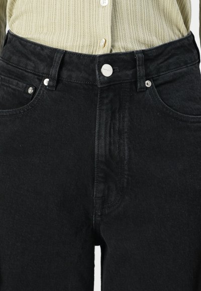 Black denim jeans feature a high waist, five-pocket design, silver button closure, and subtle texture with a slightly faded appearance.