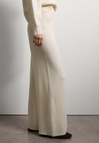 Crème-kleurige wijde gebreide broek met een zachte textuur en een geribde tailleband, gecombineerd met donkere schoenen. Strakke lijnen, minimalistisch ontwerp.