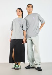 Grå, oversized t-skjorter med diskrete lilla logoer. Et svart denimskjørt med frontspalte og slitt kant kontrasterer med lyse jeans og sneakers.
