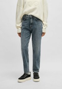 Jeans de mezclilla azul claro con cintura alta, corte recto y un ligero desgastado, combinados con zapatillas de plataforma negras y un suéter crema.