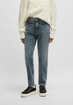 Lichtblauwe denim jeans met een hoge taille, rechte pasvorm en subtiele vervaging, kombiniert met zwarte platform sneakers en een crèmekleurige trui.