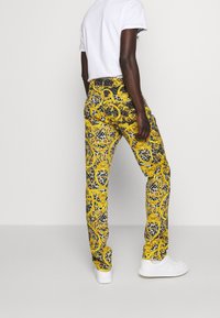 Gula och grå mönstrade byxor med ett barockmönster och djurtryck, tillverkade av ett slätt tyg och skräddarsydda med en rak passform.