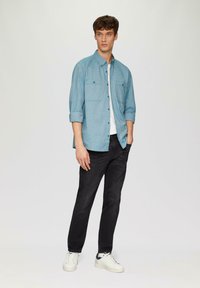 Lichtblauw overhemd met knopen, voorzien van twee borstzakken en opgerolde mouwen, gecombineerd met zwarte jeans en witte sneakers. Glad textuur, casual pasvorm.