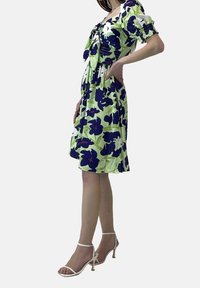 Blommönstrad klänning i grön och marinblå med puffärmar. Åtföljd av vita strapatsandaletter med hög klack. Slät tyg med en svävande design.