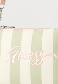 Υφασμάτινη θήκη με κάθετες ανοιχτοπράσινες και λευκές ρίγες, ροζ φερμουάρ και ροζ κεντημένο λογότυπο "Guess".