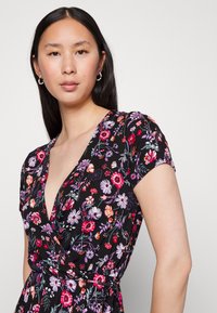 Vestido floral com fundo preto, mangas curtas e decote em V profundo. Flores em rosa, roxo e laranja com detalhe de cintura ajustada.