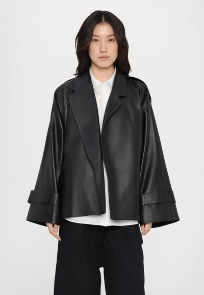 Jachetă din piele neagră cu mâneci largi și guler cu tăietură. Prezintă o textură elegantă, un design minimalist și detalii subtile la mansete.