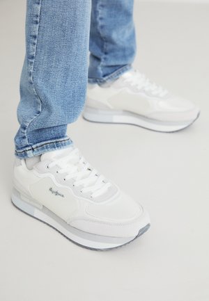 Witte sportieve sneakers met een gestructureerde, gladde afwerking, voorzien van veters en een grijze rubberen buitenzool. Gecombineerd met lichte, taps toelopende blauwe jeans.