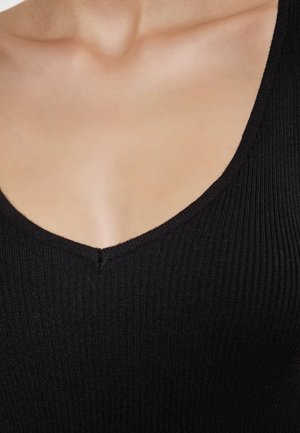 Sort ribbet tanktop med V-halsdesign. Har tekstureret stof og en ren finish ved halsudskæringen, der understreger enkelhed.