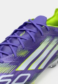 Purple soccer cleat with a textured surface, featuring white and neon green striped accents, and purple laces.