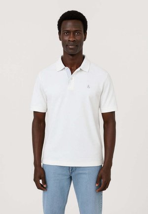 Maglietta polo bianca in cotone con colletto, maniche corte e un sottile logo della ampersand sul petto. Indossata con jeans azzurri chiari.