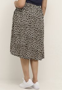 Luipaardprint midi-rok van een lichtgewicht stof, met een elastische tailleband en geplooid ontwerp, gecombineerd met witte sneakers.