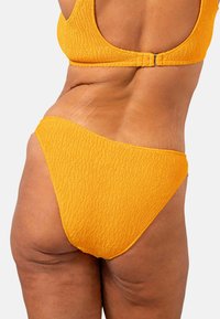 Gelber, strukturierter Bikini-Unterteil mit einer tiefen Schnittform. Enthält ein geripptes Design und eine glatte Oberfläche, geeignet für Bademode.