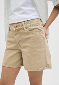 Shorts in denim beige con vita aderente, design a cinque tasche, chiusura frontale con bottone e dettagli di cucitura in vista. La texture è leggermente usurata.
