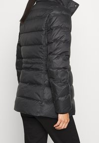 Chaqueta negra tipo plumas con cuello alto y diseño acolchado, que presenta una textura suave y brillante, y una silueta ajustada.