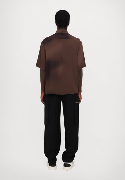 Barna, rövid ujjú ing, laza szabással és hátsó yokéval, fekete, bő szárú cargo nadrággal párosítva, amely oldzsebekkel rendelkezik, és fehér tornacipővel.