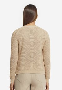 Beige gestrickter Pullover mit hexagonalem Muster, geripptem Halsausschnitt und Bündchen sowie einem leicht gekürzten Saum. Weicher Stoff und lässige Passform.