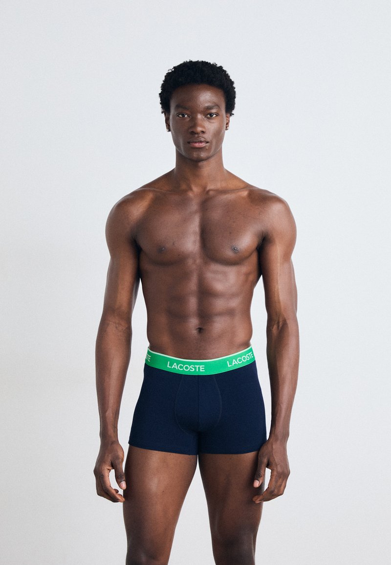Boxers bleu marine avec une ceinture en logo Lacoste verte. Le tissu semble doux et extensible, conçu pour le confort et l'ajustement.