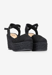 Sandalias de cuña negras con plataforma de yute tejido texturizado. Cuentan con una puntera de ante y correa ajustable al tobillo. Forro interior suave.