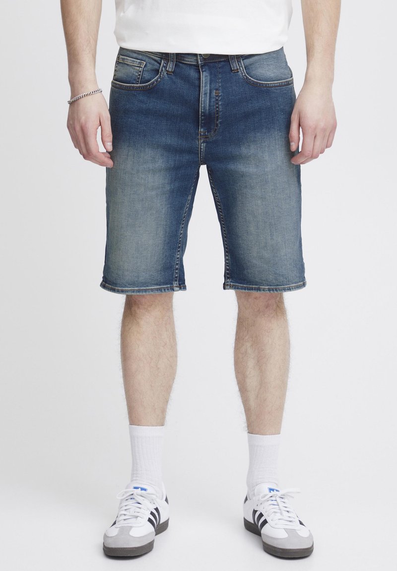 Pantalones cortos de mezclilla en azul oscuro con un efecto desvanecido, que cuentan con una cinturilla resistente, bolsillos laterales y dobladillo enrollado. Estilo combinado con zapatillas blancas.