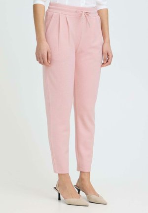 Femme portant un pantalon fuselé rose clair avec des plis et une taille à cordon, associé à des talons slingback beige à bout pointu.
