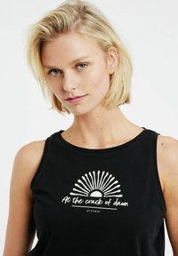 Canottiera nera senza maniche con grafica di sole bianco e raggi, con il testo "All'alba" centrato sotto. Materiale in cotone morbido, vestibilità casual.
