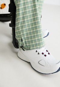 Groene geruite broek met een gestructureerde afwerking, voorzien van een rits aan de zoom, gecombineerd met witte sportschoenen met gekleurde accenten.
