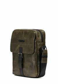 Torebka listonoszka w oliwkowo-zielonym kolorze, z klapką, zapinana na zamek, z czarnym paskiem i gładką teksturą. Posiada naszywkę markową z przodu.