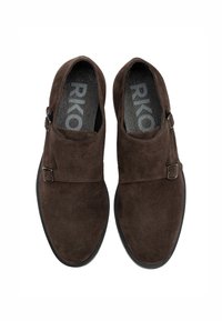Bruna mockaskinns slip-ons med rund tå, prydda med en sidobuckle och en texturerad inläggssula, placerade på en svart gummisula.