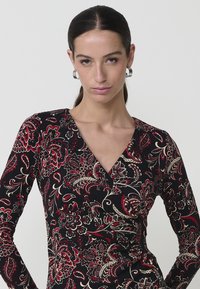 Vestido negro con patrón floral rojo y dorado, de manga larga, diseño en envoltura y deep V en el cuello. Tejido suave y elástico con una silueta ajustada.