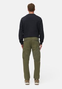 Schwarzer Sweatshirt mit Rundhalsausschnitt, kombiniert mit olivgrünen Cargo-Hosen mit seitlichen Taschen und einem leicht lockeren Schnitt. Braune Schuhe sind sichtbar.