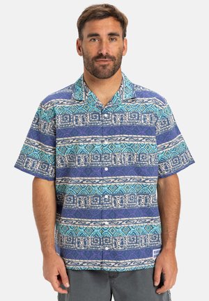Camisa de botones de manga corta en azul y púrpura con intrincados patrones geométricos y florales, hecha de una tela ligera con un corte relajado.