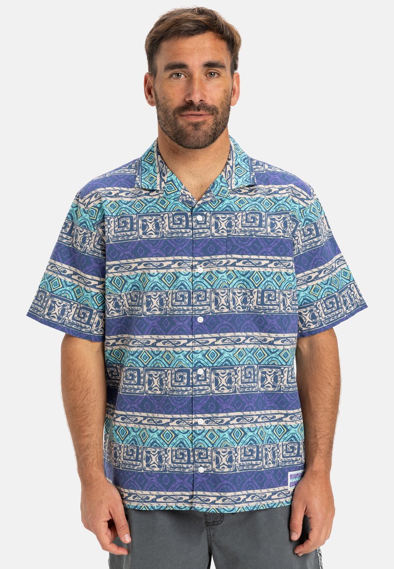 Camisa de botones de manga corta en azul y púrpura con intrincados patrones geométricos y florales, hecha de una tela ligera con un corte relajado.