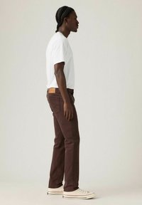 Bruna jeans i denim, vit T-shirt och vita sneakers. Jeansen har en etikett på bakre midjebandet. Raka ben, minimalistisk design.