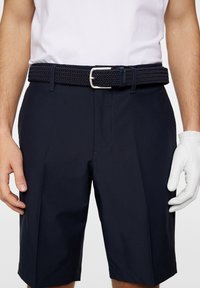 Mörk marinblå golfshorts med ett texturerat, flätat bälte. Shortsen har rak skärning och är tillverkade av lättviktig tyg. Vit handske synlig.