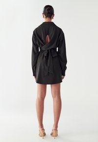 Mustmustern, mille varrukatega ja vöökohaga. Omab selja lõhet ja sileda tekstuuri, ulatudes üle põlvede. Heleda taustaga.