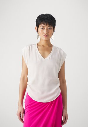 Blusa rosa chiaro con scollo a V e maniche corte a kimono, realizzata in tessuto morbido e liscio; indossata sopra una gonna rosa brillante.