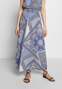 Longue jupe maxi bleue avec un motif cachemire, ceinture élastique, tissu fluide et associée à des sandales noires à lanières.