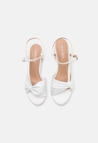 Sandali bianchi open-toe con un dettaglio in tessuto annodato sulla parte anteriore, cinturino alla caviglia regolabile e finitura liscia simile alla pelle.