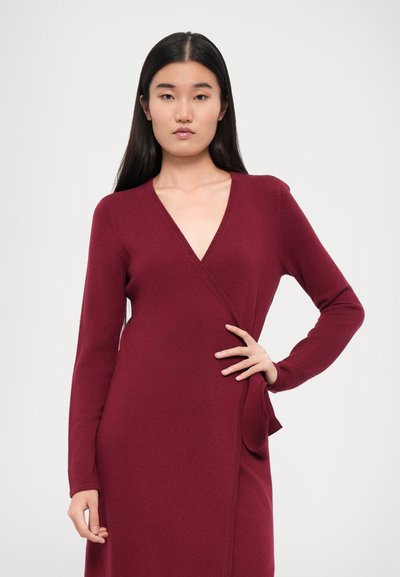 Burgundy wrap dress with long sleeves, V-neckline, and a side knot detail. Soft texture with a fitted silhouette.